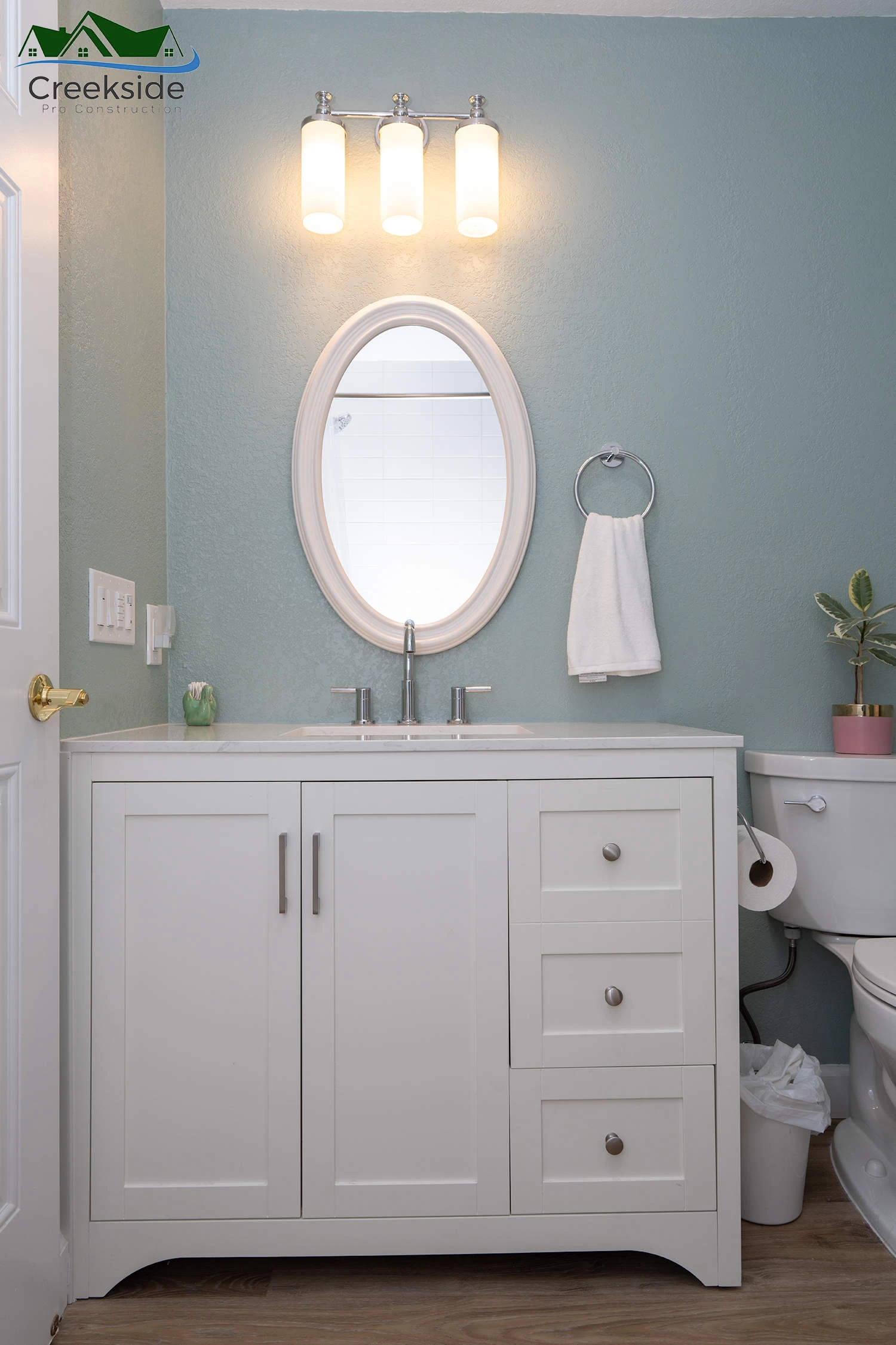 A modern bathroom with a white vanity, oval mirror, and three lights above.