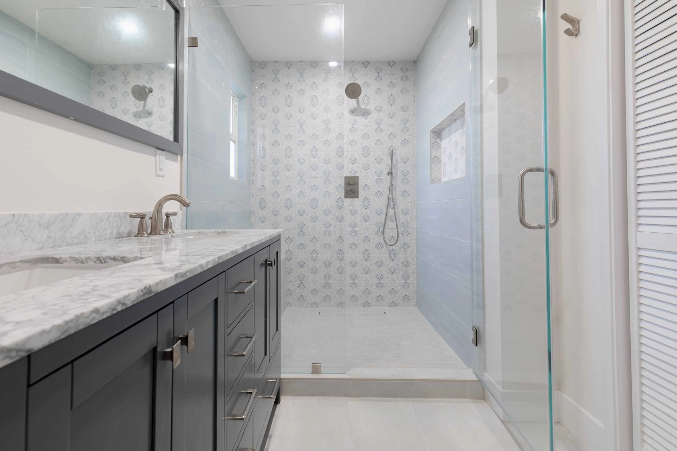Modern Bath Room Design – Contra Costa County, CA Modern bathroom with a marble-topped vanity, large mirror, glass-enclosed shower, and patterned tile feature wall, perfectly crafted by expert home remodelers.