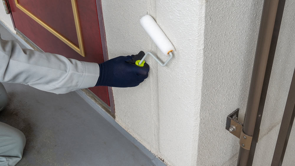 A person painting a white wall with a paint roller near a red and gold door, setting the stage for an impressive home remodeling project.