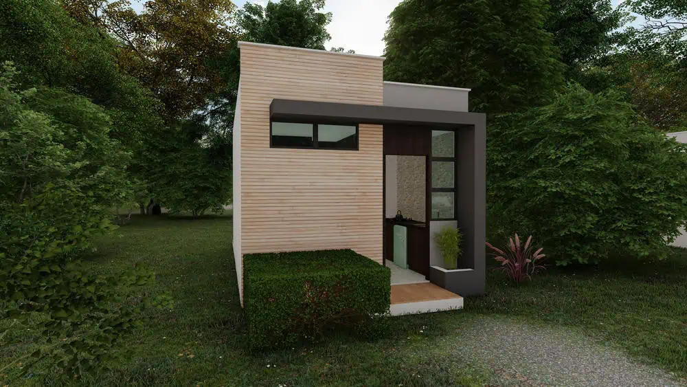 A small, modern tiny house with light wood siding and large windows, surrounded by lush greenery on a grassy plot. Perfect for a cozy retreat or to inspire your next project if you're a home remodeler.