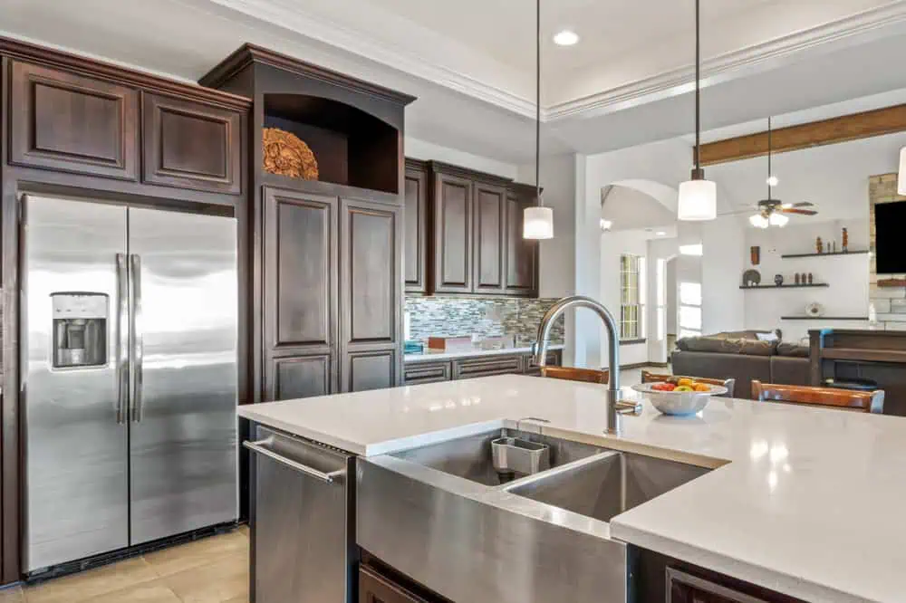 Modern kitchen with dark wood cabinets, stainless steel appliances, large island with a farmhouse sink, pendant lighting, and fruit bowl on counter. Perfect for anyone considering home remodeling.