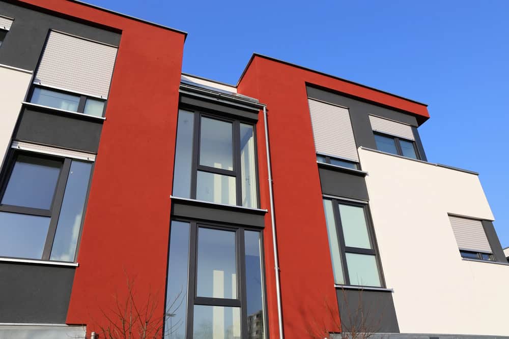 Modern apartment building with red and white facades, large windows, and balconies under a clear blue sky, perfect for those seeking contemporary living spaces or planning a kitchen remodeling.